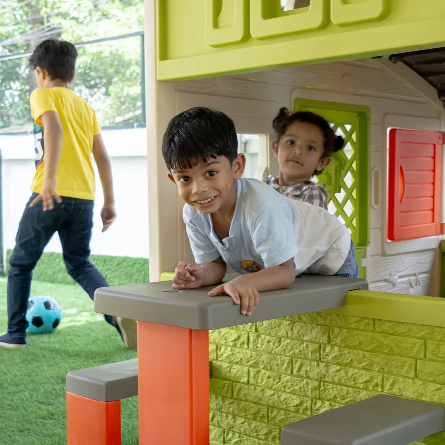 Smiling boy at the playhouse with a friend peeking from behind